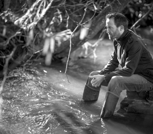 Actor Nik Howden posing in a stream in Wotton-under-Edge by Paul Groom